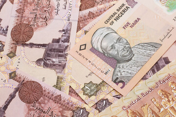 A close up image of a peach colored, five Nigerian naira bank note on a background of Egyptian one pound bank notes