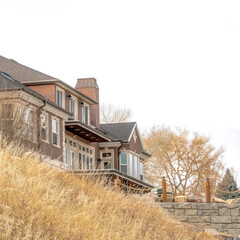 Square crop Grassy hill with huge houses and retaining wall against cloudy sky background