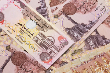 A close up image of a five dirham bank note from the United Arab Emirates on a background of Egyptian one pound bank notes in macro