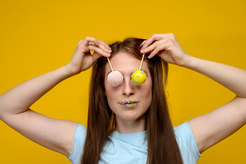 young european woman playes with cake pops on yellow background