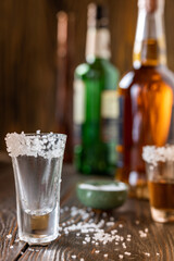 An empty tequila glass, with salt at the edges, stands on the bar, in the background are different bottles of alcohol, shallow depth of field, selective focus. The concept of a drink in the bar.