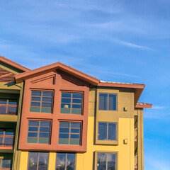 Square Home exterior with balconies and multi color walls against blue sky and clouds