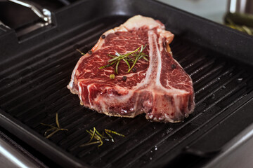 Fresh steak cooking at griddle pan. Closeup raw beef with rosemary grill at pan.