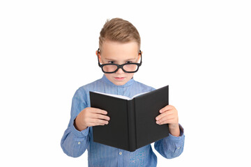 Fototapeta premium Cute dreamy schoolboy reads book and wearing glasses while standing in the studio, isolated over white