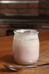 Yogurt in open small glass jar with spoon on wooden cutting boar