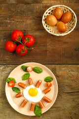 Fried eggs with sausages in the shape of a sun. Children's breakfast next to eggs and tomatoes.