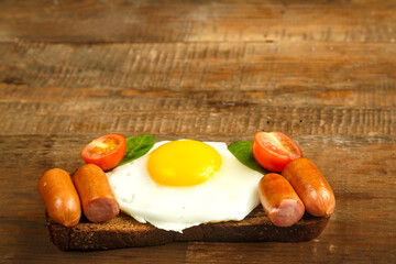 Fried egg with sausages and tomatoes on a piece of bread on a wooden table.