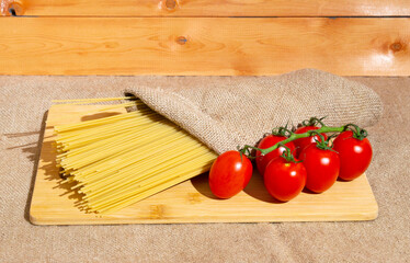 spaghetti and a branch with tomatoes on a background of burlap. rustic view, atmosphere.