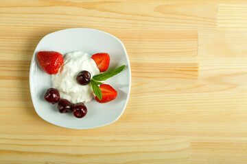 Ice cream dessert with strawberries and cherries in a plate on a wooden table. Copy space.
