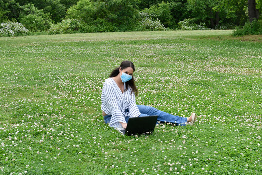 Beautiful young woman with laptop computers park, with a protective face mask