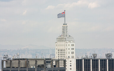 Topo do edifício Altino Arantes, com a bandeira do Estado de São Paulo ao vento e a cidade no...