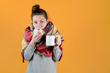 A young woman with a hot drink wrapped in a blanket wipes her nose with a napkin