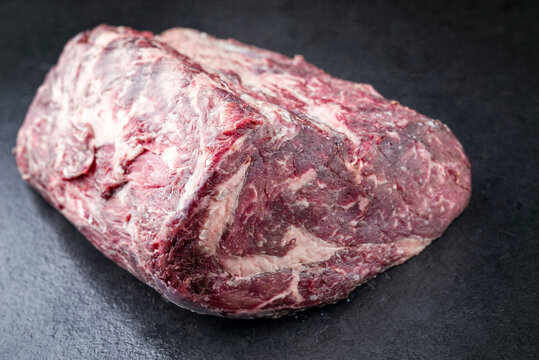 Raw dry aged Kobe rib-eye steak roast offered as close-up on a black board