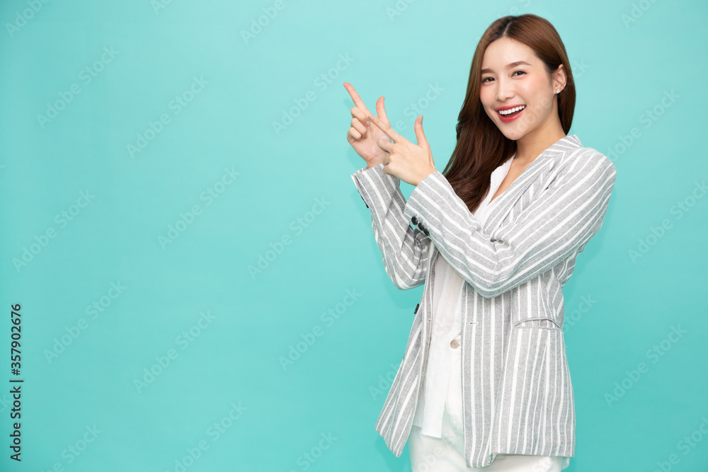 Wall mural young asian woman smiling and pointing finger to empty copy space isolated on green background