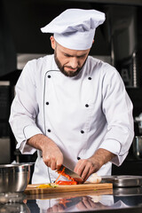 Chef man with knife at restaurant kitchen. Chef male slicing pepper.