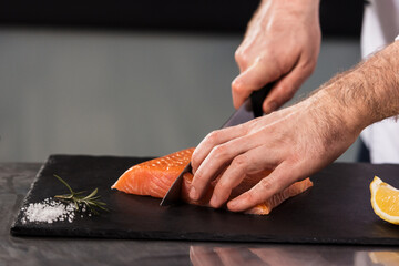 Chef hands cut salmon fillet. Closeup male hands slice fresh fish.