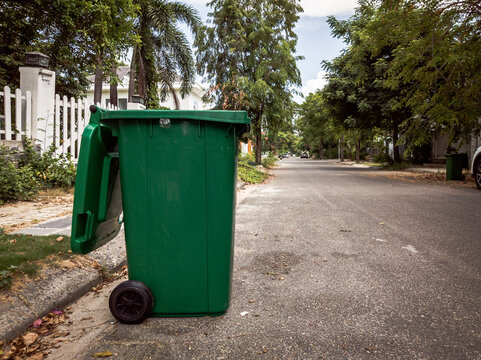 Opened big empty green plastic trash garbage bin in front of the modern house with green trees. No public trash on the side of the road. Infectious control, garbage disposal, disposal of waste concept