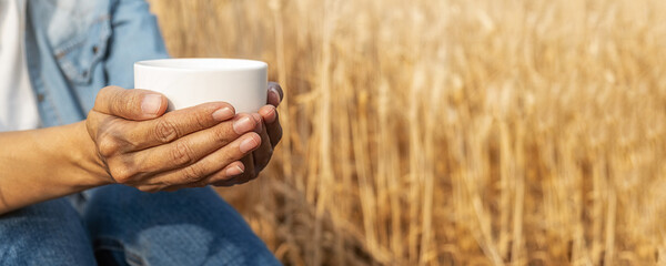 Asian woman holding cup of coffee and sitting in barley field on summer. Relaxing concept.