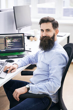 Cheerful senior programmer developer working in IT office, sitting at desk and coding, working on a project in software development company or startup. High quality image.