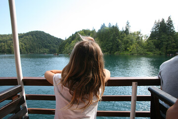 Back view of a blonde haired child leaning on a fence watching the lake in Plitvice National Park in Croatia.