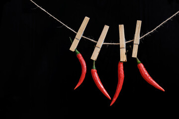 Red hot peppers hang on a clothespin on a rope on a black background. Hot spice. Close-up.