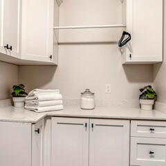Square crop Laundry room of home with white wood cabinets and clothes rod against wall