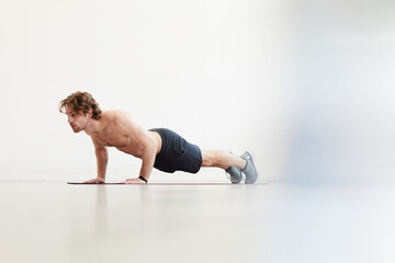 Obraz premium Shirtless young man doing push-ups on the floor against the white background