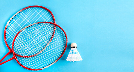 Sport flat lay with two rackets and shuttlecock for playing badminton on blue background. Concept healthy lifestyle. Top view. Copy space. Banner.