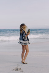 Girl in ethnic dress on a white sand beach is dancing with fruit in her hands. Against the background of the ocean