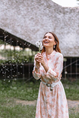 Fototapeta premium A girl in a light dress, blowing on dandelions