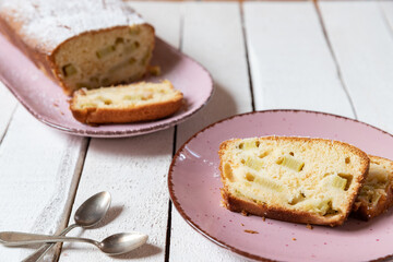 geschnittener, frischer Kuchen mit Rhabarber, Puderzucker und Eierlikör auf einem Tisch aus Holz in der Küche am Nachmittag