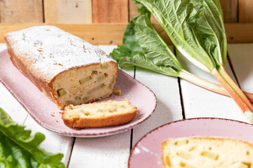 geschnittener, frischer Kuchen mit Rhabarber, Puderzucker und Eierlikör auf einem Tisch aus Holz in der Küche am Nachmittag