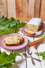 geschnittener, frischer Kuchen mit Rhabarber, Puderzucker und Eierlikör auf einem Tisch aus Holz in der Küche am Nachmittag