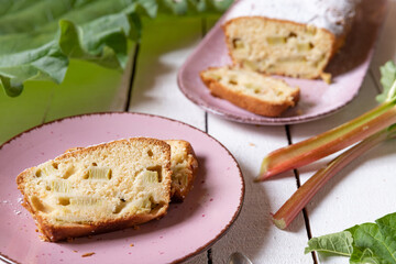 geschnittener, frischer Kuchen mit Rhabarber, Puderzucker und Eierlikör auf einem Tisch aus Holz in der Küche am Nachmittag