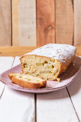 geschnittener, frischer Kuchen mit Rhabarber, Puderzucker und Eierlikör auf einem Tisch aus Holz in der Küche am Nachmittag