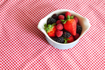 Fresh food berries, raspberries, blackberries and strawberries in a vintage bowl on red and white gingham fabric background shot from above with room for copy space