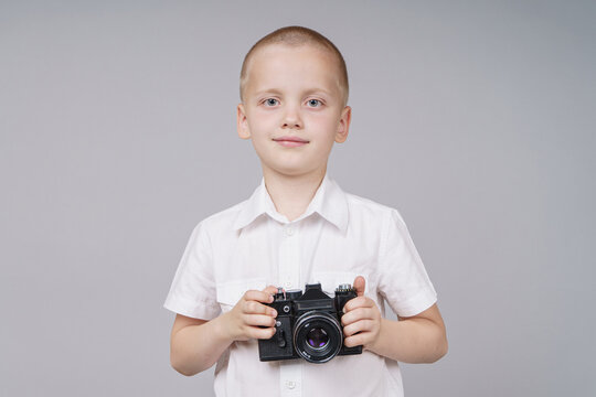 Child boy with retro compact camera, isolated on gray background.