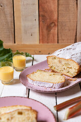 geschnittener, frischer Kuchen mit Rhabarber, Puderzucker und Eierlikör auf einem Tisch aus Holz in der Küche am Nachmittag