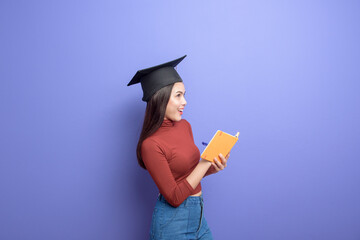 Portrait of young University student woman with graduation cap on violet background