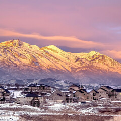 Fototapeta na wymiar Square Homes on snowy hill against frosted Wasatch Mountain with golden glow at sunset