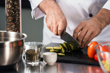 Male hands cut food at kitchen. Closeup chef hands cut cucumber.