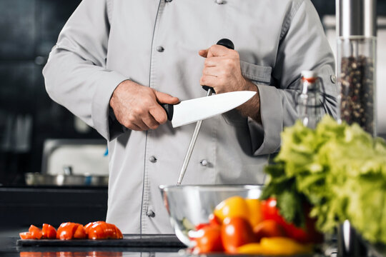 Chef man sharpen knife at kitchen restaurant. Male professional sharpen knife.