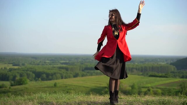 Georgian woman dances national dance in red national dress on the green hills of Georgia background. Georgian culture lifestyle.
