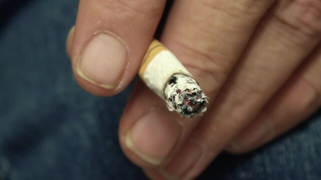 eine qualmende Zigarette in der Hand von einem Raucher