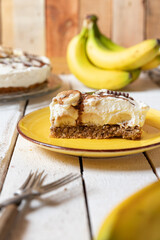frisch gebackene Torte mit Bananen, Sahne, Schokosoße, Karamellsoße und Haselnussboden auf Tisch aus Holz in der Küche zum Kaffeetrinken
