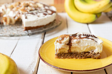 frisch gebackene Torte mit Bananen, Sahne, Schokosoße, Karamellsoße und Haselnussboden auf Tisch aus Holz in der Küche zum Kaffeetrinken