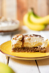 frisch gebackene Torte mit Bananen, Sahne, Schokosoße, Karamellsoße und Haselnussboden auf Tisch aus Holz in der Küche zum Kaffeetrinken