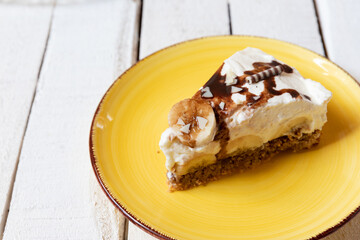 frisch gebackene Torte mit Bananen, Sahne, Schokosoße, Karamellsoße und Haselnussboden auf Tisch aus Holz in der Küche zum Kaffeetrinken