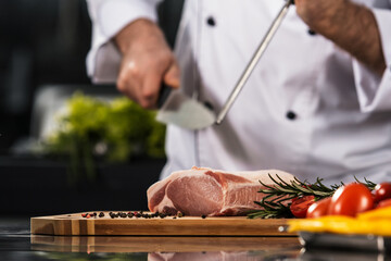 Obraz premium Chef hands with knife and beef at kitchen. Closeup chef man hands with knife.