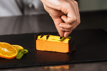 Chef hands decorate orange cake. Closeup hands decorate dessert with chocolate.